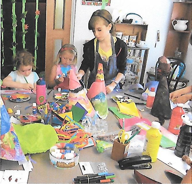Children with painting and collage materials around a table at the Tuftydawn Designs studio.
